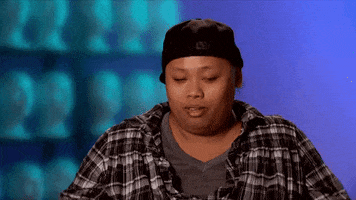 Reality TV gif. Wearing a flannel and a backward baseball cap, Jiggly Caliente on RuPaul’s Drag Race slaps both hands to her head and shakes her head in dismay.