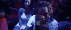Music video gif. Fetty Wap in his music video My Way, wearing driving gloves and rapping with fists in the air, in a moody room filled with party people.