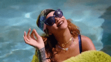 Music video gif. From the video for Bitch Better Have My Money, Rihanna chills in a swimming pool and looks up, smiling and waving hello.