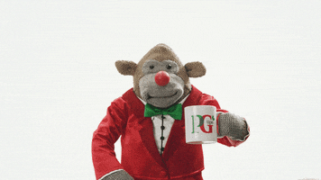 Video gif. A monkey puppet wearing a red suit raises up a mug and smiles.