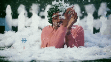 Celebrity gif. Wearing a leafy green wig and buried in the ground up to his chest, Tyler the Creator flails as he is covered in snow. A small sign with a picture of a blue snowflake is stuck in the ground next to him.