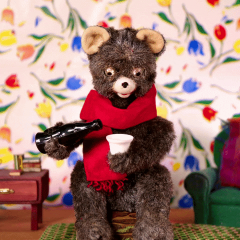 Stop motion gif. Teddy bear wearing a red scarf fills a Styrofoam cup with liquid from a brown bottle and knocks the entire drink back, its eyes wide and unblinking.