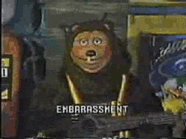 Video gif. An animatronic bear holds a banjo with a bird on the neck of it. He looks away and covers his face with his arm. Text, “Embarrassment.”