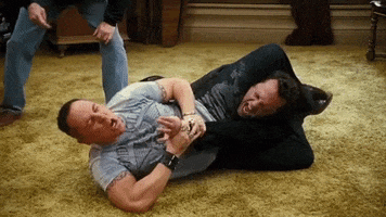 Movie gif. Jon Favreau as Denver in Four Christmases shouts while pinning Vince Vaughn as Brad in a chokehold on the floor, with his legs wrapped around Brad's neck and his hands around Brad's wrist.