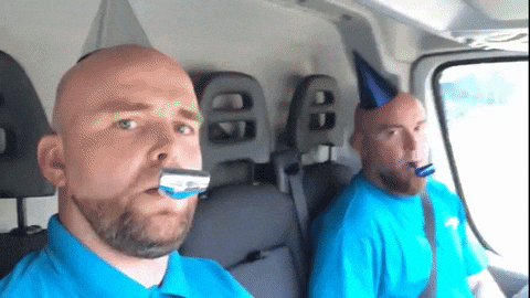 Gif se dvěma muži s narozeninovými čepičkami a frkačkami, jedoucí v autě.
